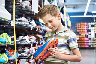 A young boy is looking at blue and orange football boots in a shoe shop.