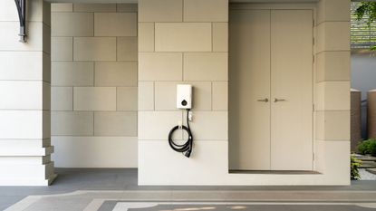 An electric car charging point mounted to a wall at a home under a car point beside a door