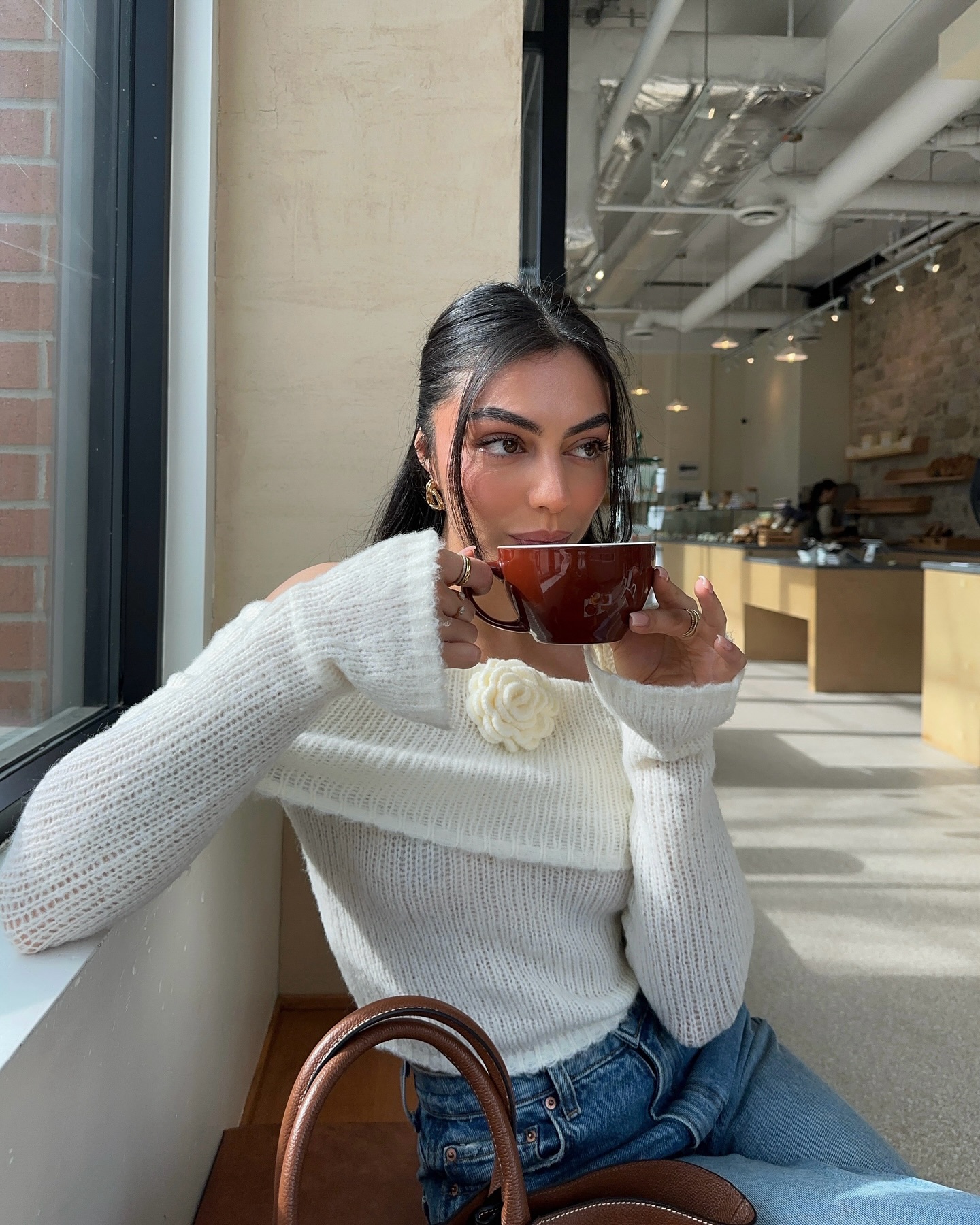 Mobina Peiman wears a white, off-the-shoulder sweater at a coffee shop.