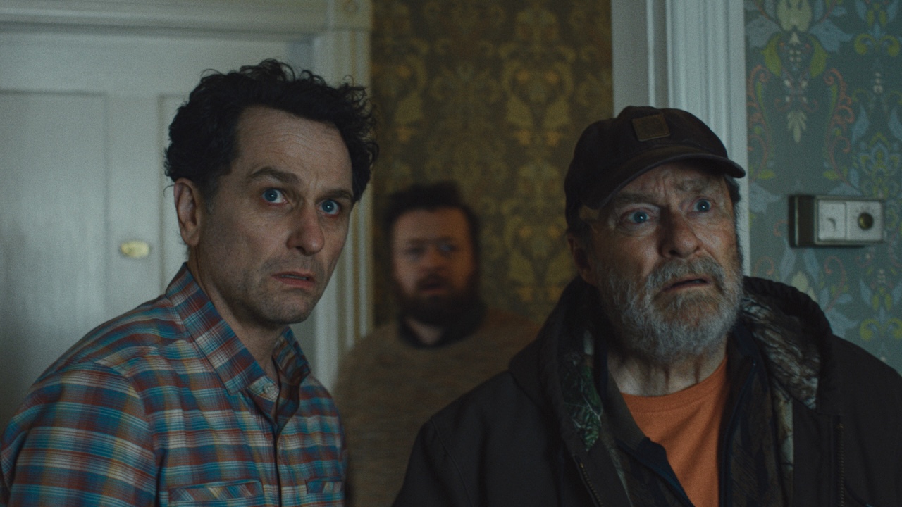 Mayor Loftis and Wyck looking wide-eyed into a hotel room in Widow's Bay Season 1