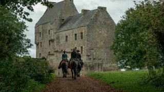 Jamie and Claire riding on horseback towards a big castle 