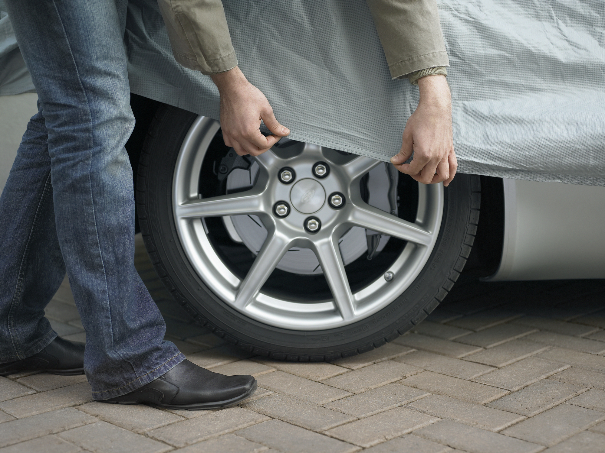 A man is stretching a fabric car cover over his car.