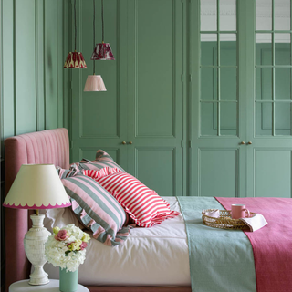 A green bedroom with pink bed and layered bedding and hanging pendants from ceiling