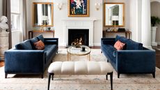 formal living room with two blue sofas and a white ottoman in front of a fireplace with a glass coffee table