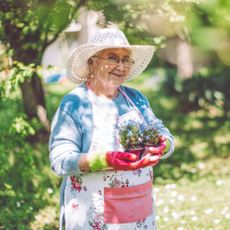 mature woman wearing hat and gardening gloves in garden with plants
