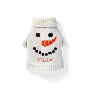 A white knitted dog sweater with a snowman's face on the front and an embroidered 'Stella' name in orange, for Christmas sweaters for dogs. 