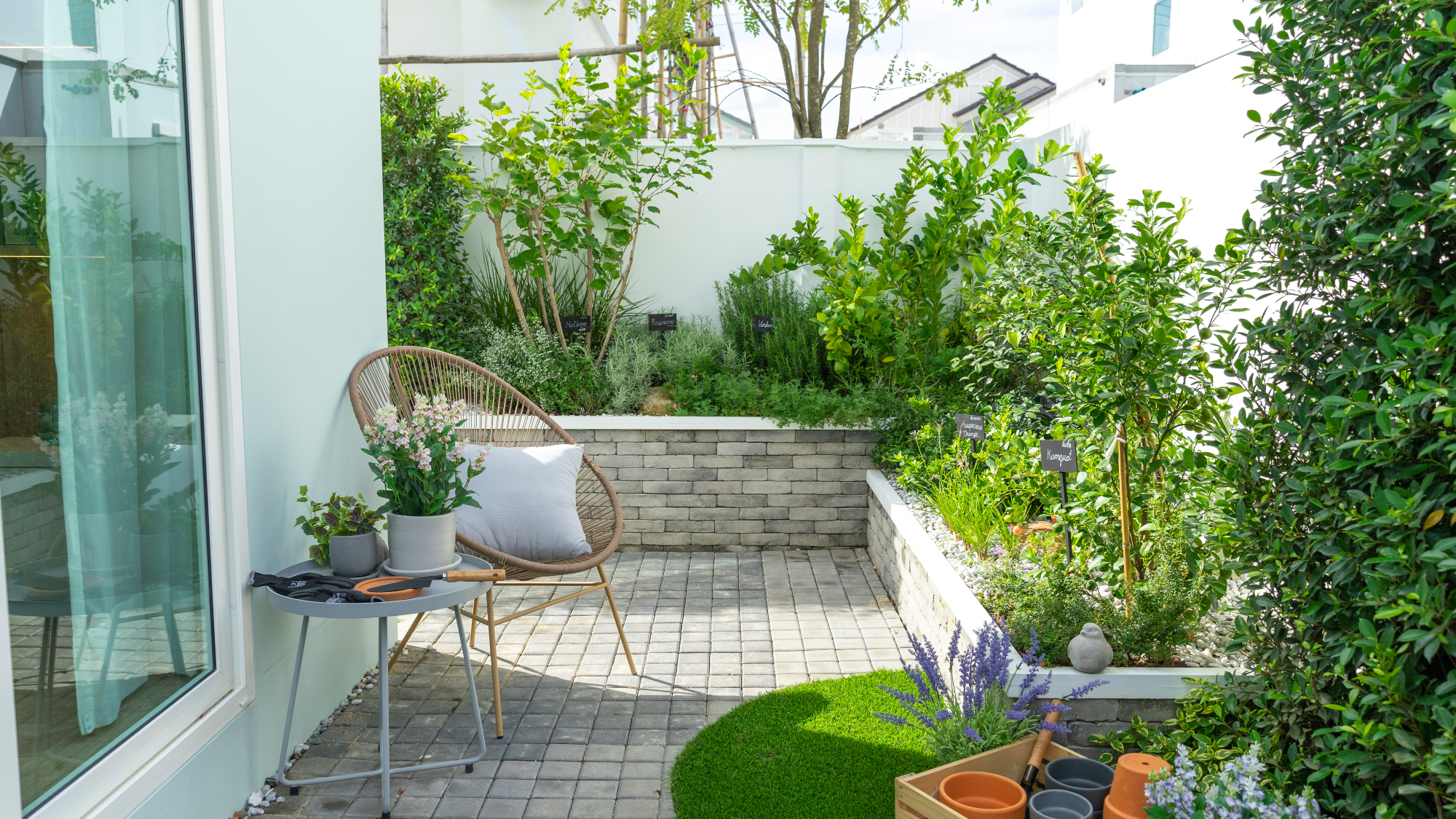 small garden patio with planted borders on low garden walls, table, chair and gardening tools and pots
