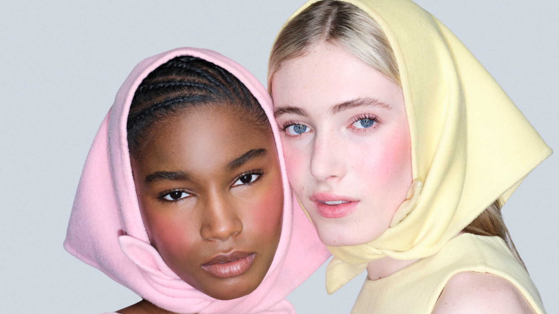 two models pose with their faces next to each other. one is wearing a pink scarf, the other is wearing yellow