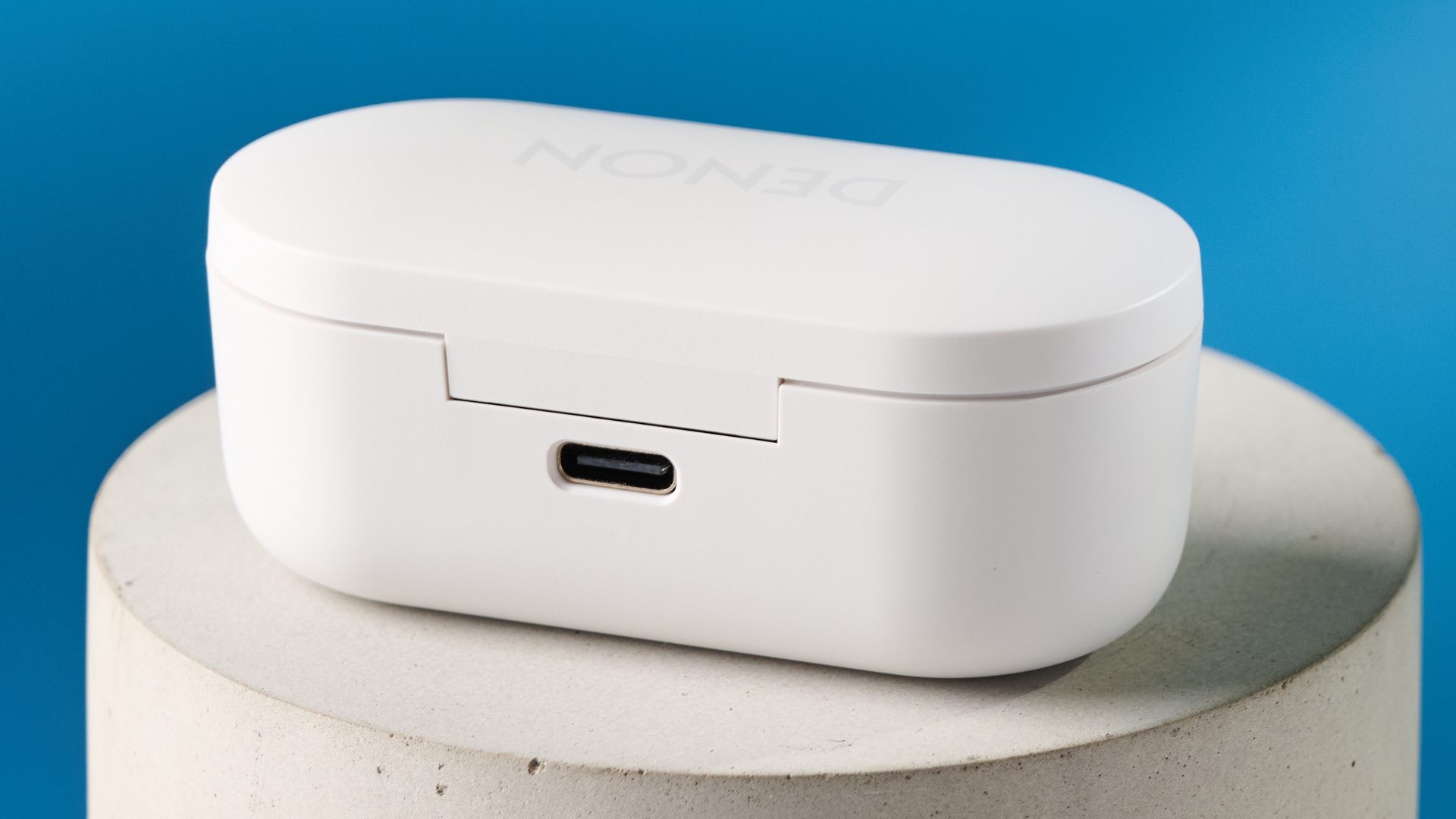 the denon perL Pro wireless earbuds in white, with circular earbud shapes, and a white charging case, photographed against a blue background