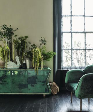 Living room with green walls, dark wooden flooring, green art deco sideboard and armchair.