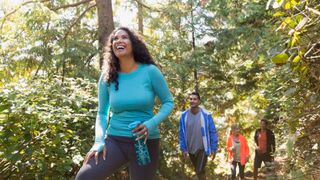 Woman laughing and smiling, holding a water bottle and walking with family and friends through woodland on a hike after learning how much weight can I lose in a month
