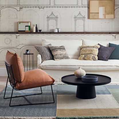 A white sofa in a living room with a black accent chair with burnt orange cushions and a circular black coffee table