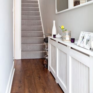 A hallway with a staircase and a radiator cover used as a shelf