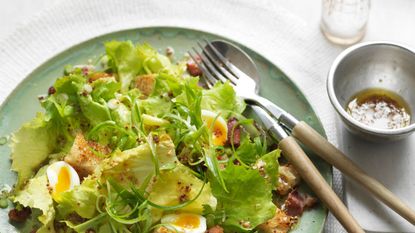 Plate of egg salad with cutlery and bowl of dressing on the side