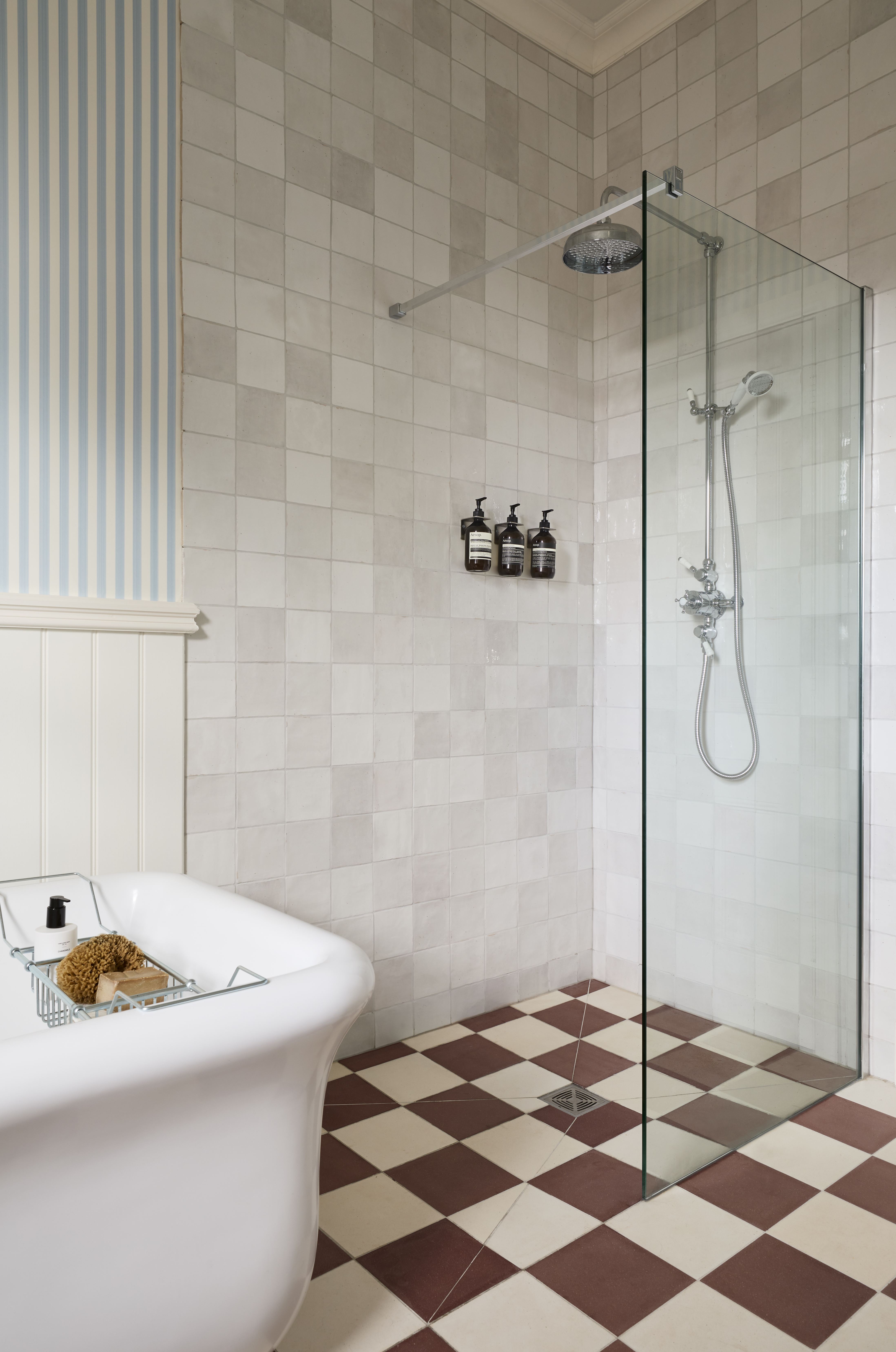 salle de bain avec baignoire blanche, papier peint à rayures bleues et blanches, carrelage à carreaux, douche à l'italienne
