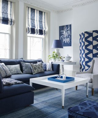 A monochromatic white and blue living room with blue sofas, white coffee table, printed screen and a woven rug