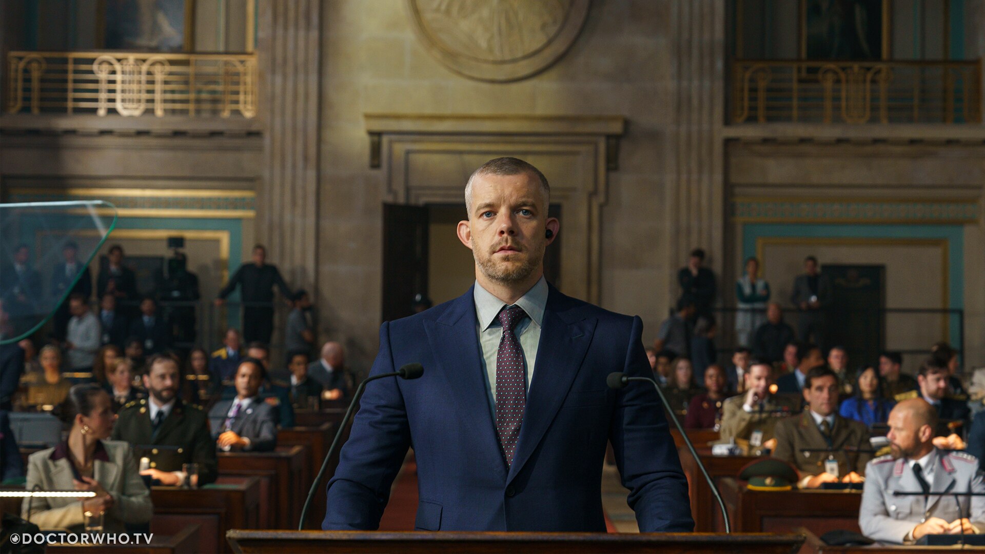 Promotional material for &quot;The War Between the Land and the Sea&quot; showing Russell Tovey as Barclay, standing in court wearing a blue suit.