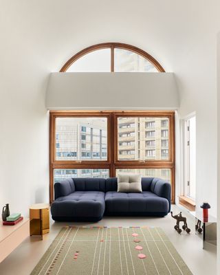 The Quilton sofa by Doshi Levien for Hay in blue, photographed at the Barbican in London against a wide window from which the building's architecture is visible