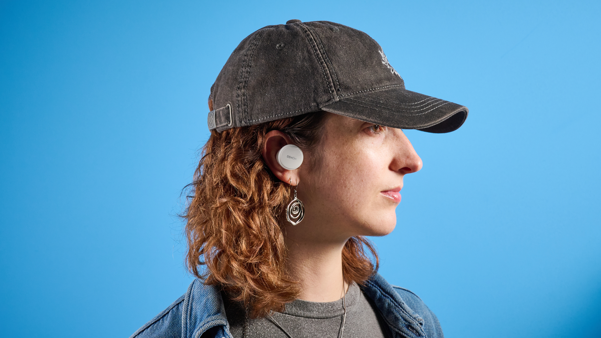 the denon perL Pro wireless earbuds in white, with circular earbud shapes, and a white charging case, photographed against a blue background