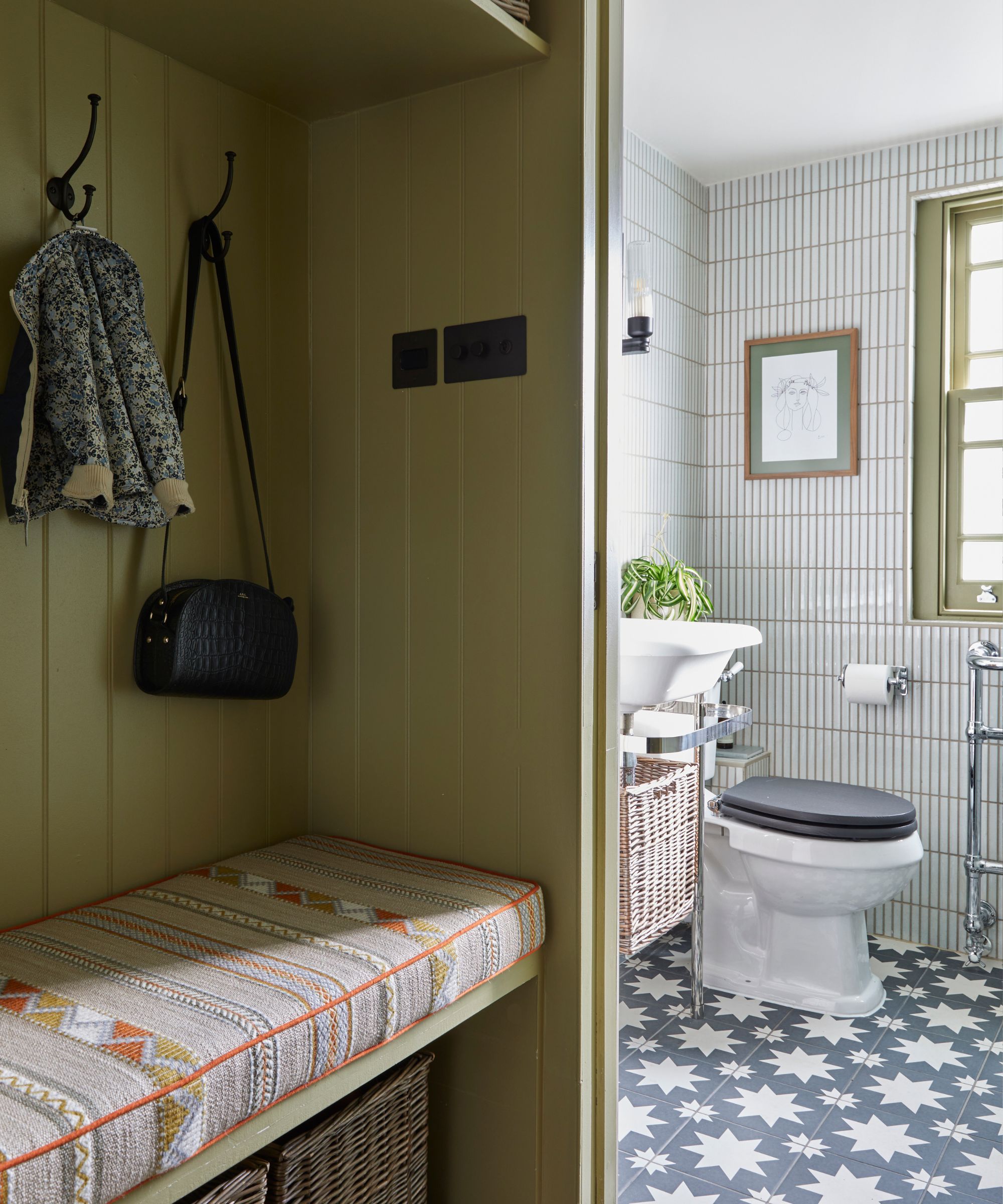 A bathroom with blue patterned tile on the floor and white vertical tile on the walls, with a view from an olive green room