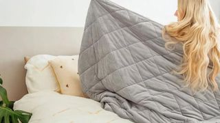 Blonde woman in bed with a grey Kudd.ly Weighted Blanket