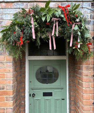 Christmas foliage arch above a green door with red and pink bows