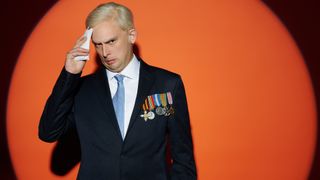 Kieran Hodgson as an older Prince Andrew in front of an orange backdrop for Prince Andrew: The Musical