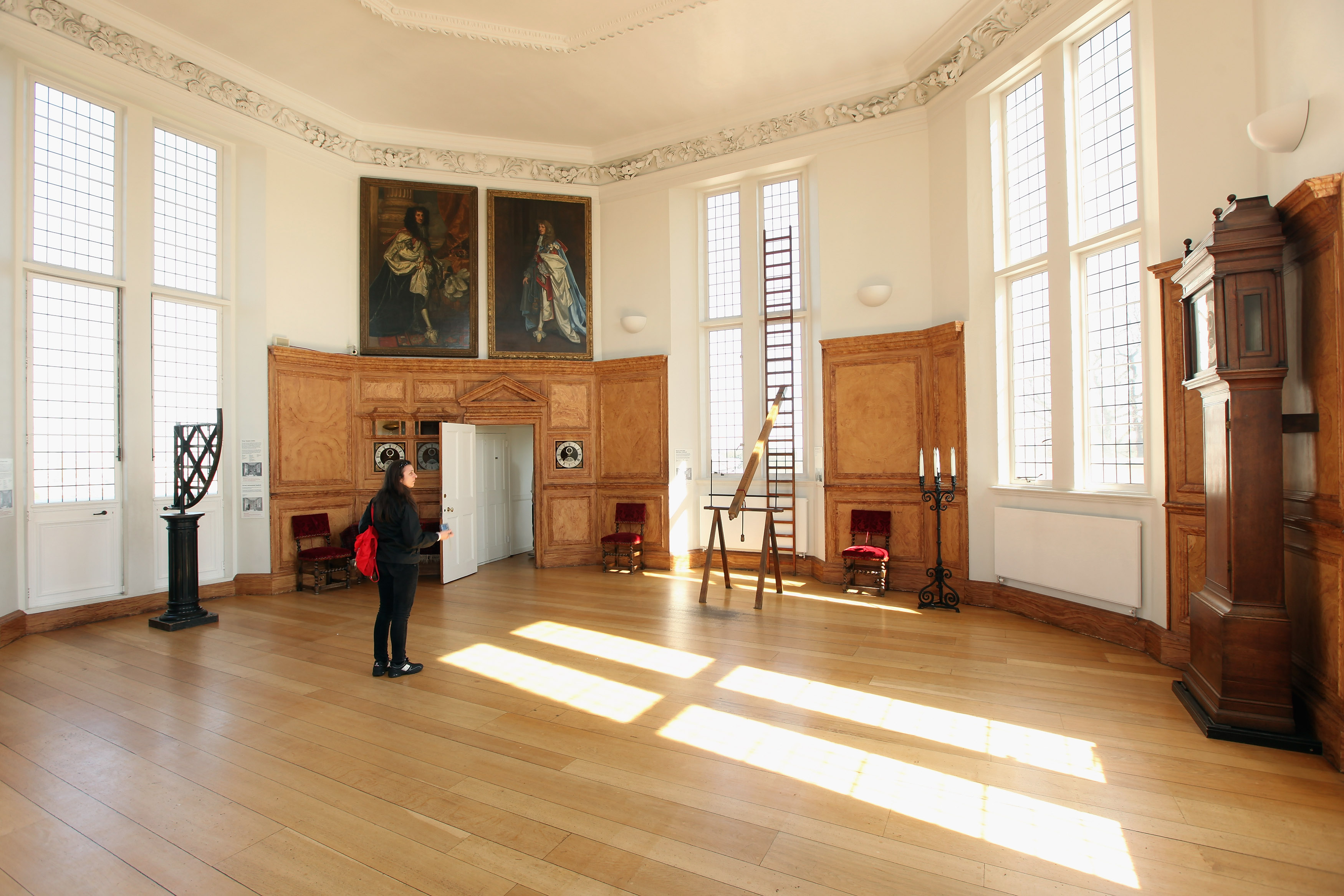 A man stands in a large room with many windows and a wooden floor