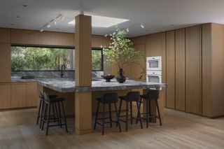 A modern, minimalist kitchen with wooden walls, grey marble countertops and a large island