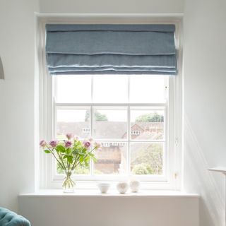 Large white window with blue blinds and flowers on top of windowsill