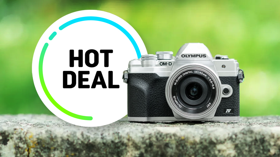 A silver and black Olympus OM-D E-M10 Mark IV camera sits on a stone ledge. Beside it, a circular graphic with "Hot Deal" in bold black text on a white background