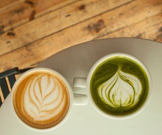 A cup of matcha and a cup of coffee on a countertop
