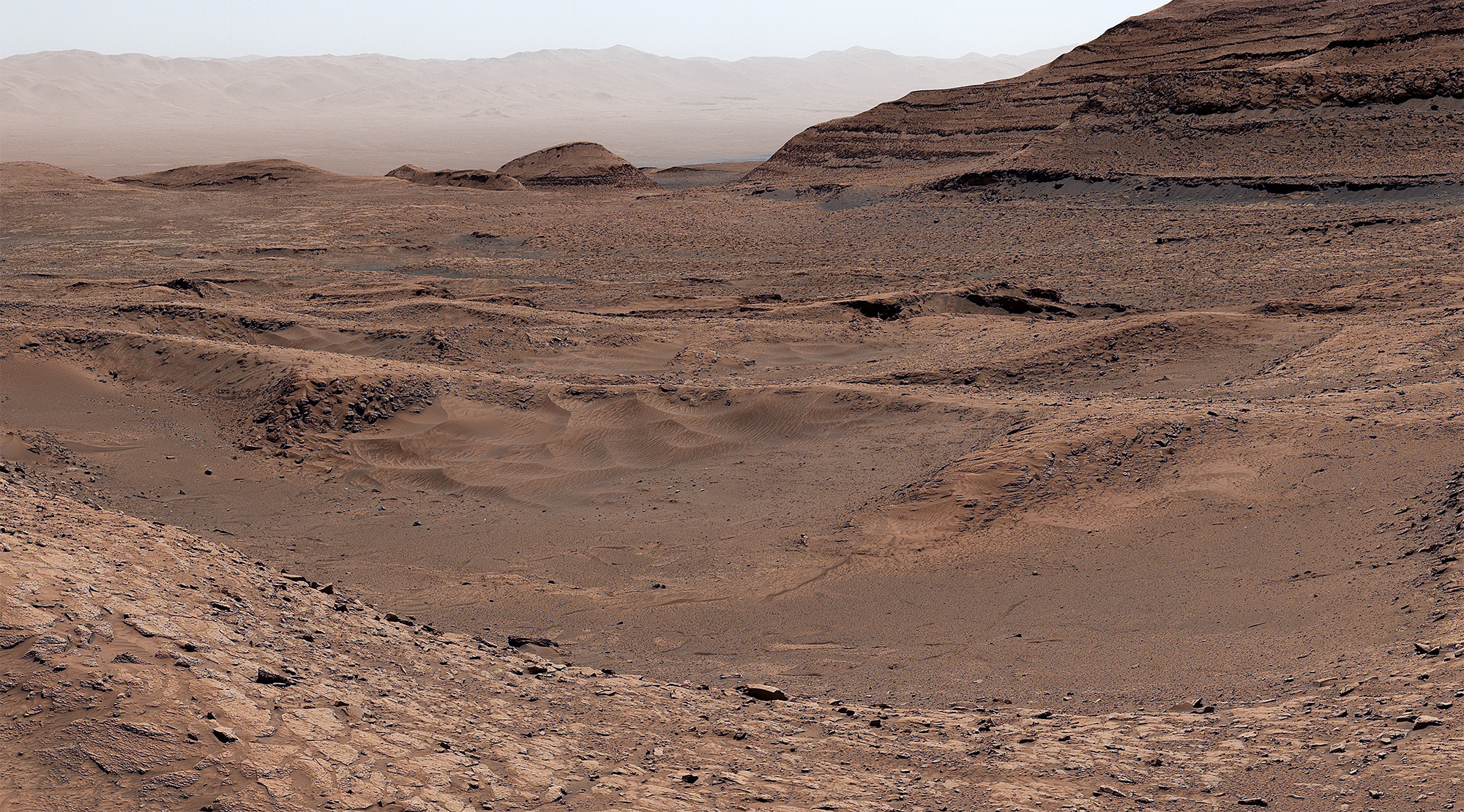 A reddish-brown landscape with dunes in the distance
