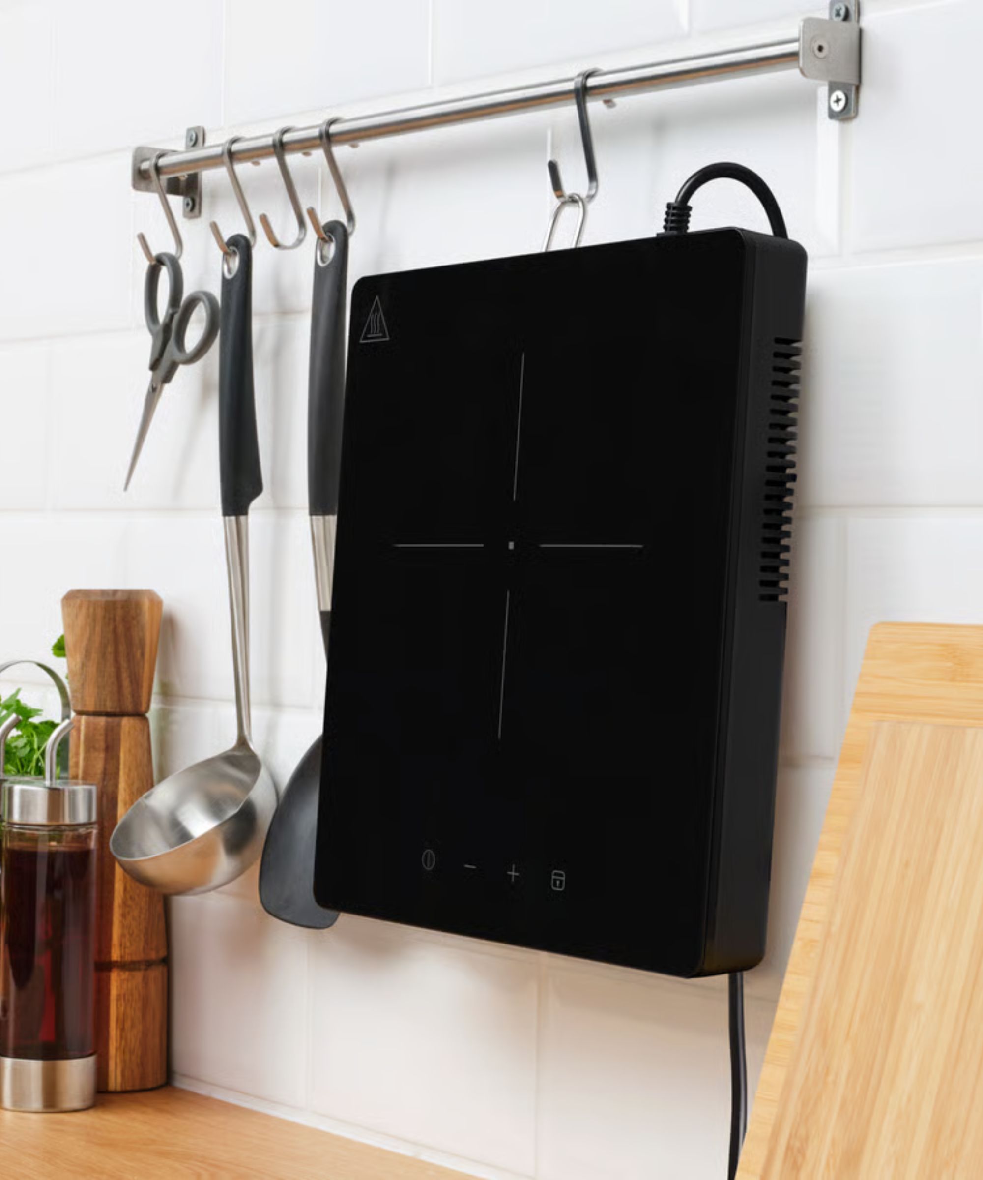 A black single burner electric stovetop hanging from a metal hook against a white subway tile wall.