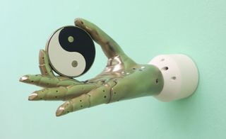 A prosthetic hand attached to a wall the thumb and first finger holding a circular disc with a ying/yang symbol.