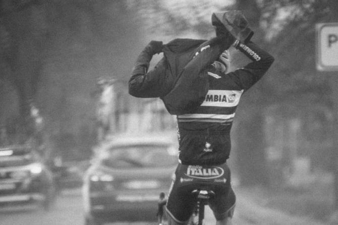 A rider tries to get his rain jacket on during a downpour and strong winds.