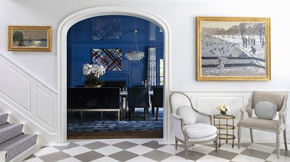 A white entrance hall with grey and white checkered floor and entrance to blue dining room