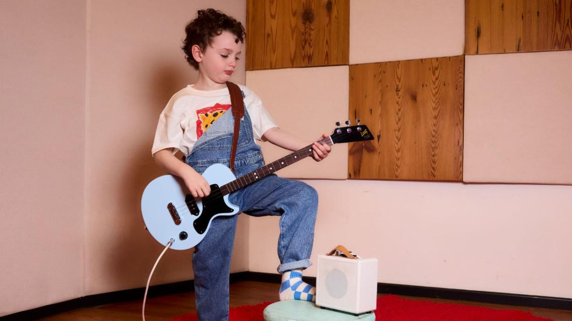 A photo of a child playing a Gibson x Loog guitar.