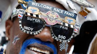 An IndyCar fan with IndyCar-themed glasses and a patriotic blue moustache watches the legendary IndyCar 500 race.
