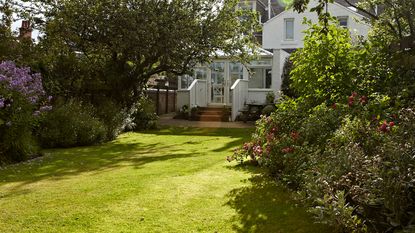 Lawn bordered by flower beds and hedges leading to garden room