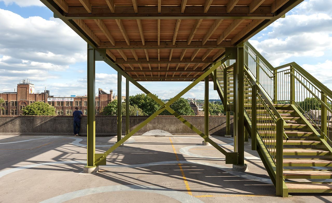 Top level of a carpark, with a man looking over the wall to the city beyond