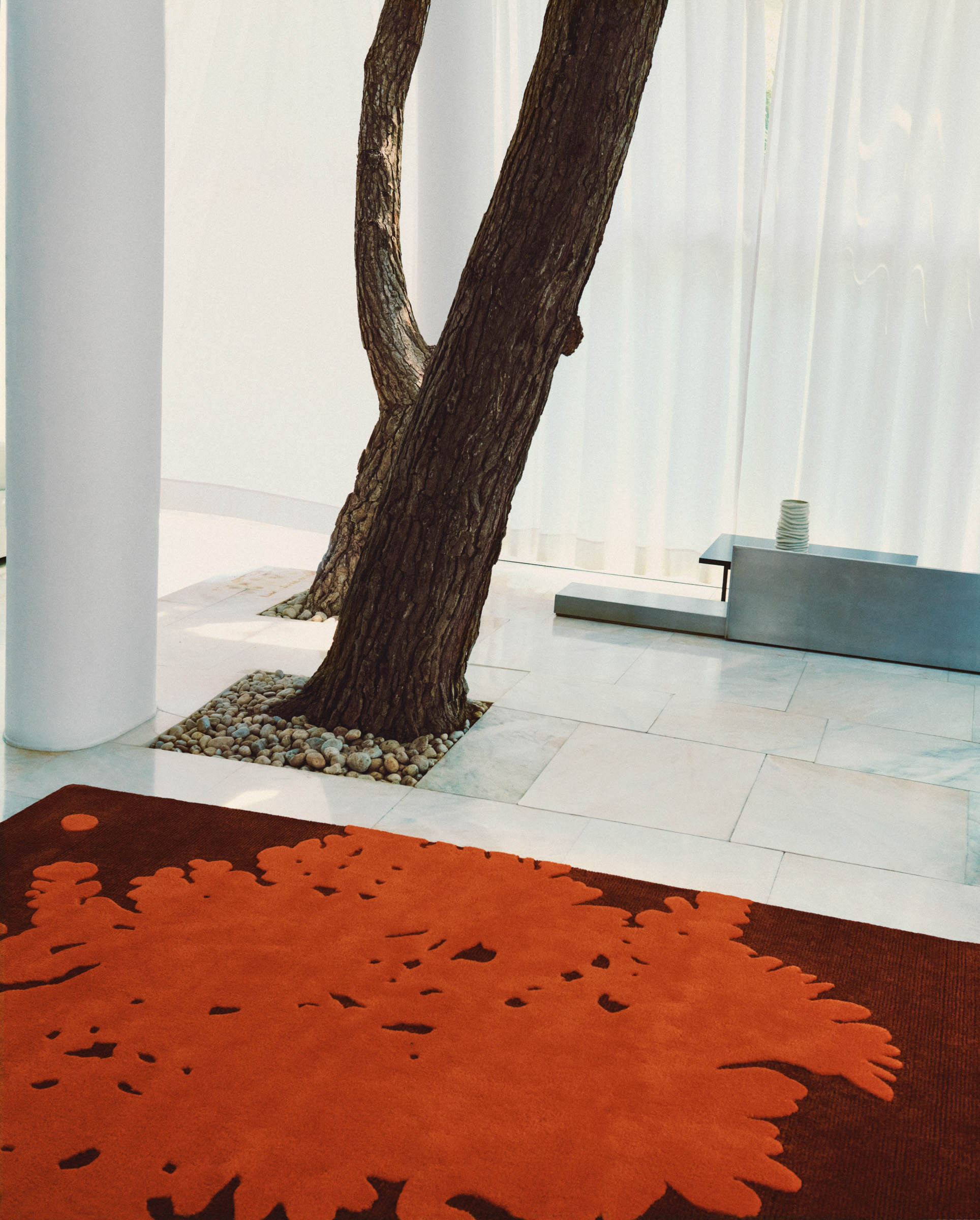 red textile wall hanging in tiled room with tree trunks