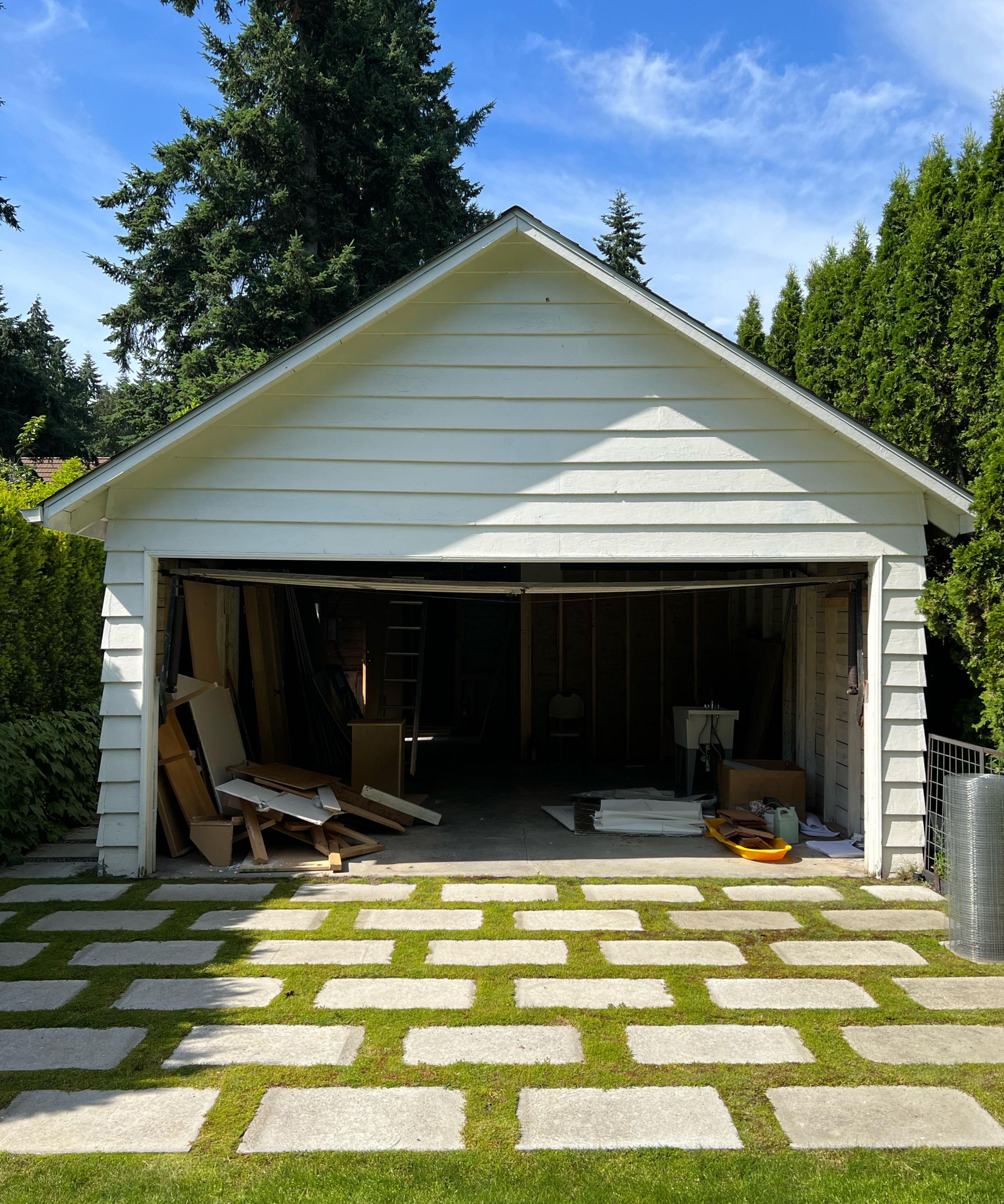 the 'before' image of a white shiplapped garage in a designers garden with grass and stone stepping stones