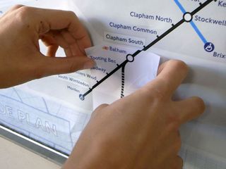’Northern Line extension sticker #fnideqbranch’ by Asif Khan and Pernilla Ohrstedt. Two hands sticking a route to a map on a wall.