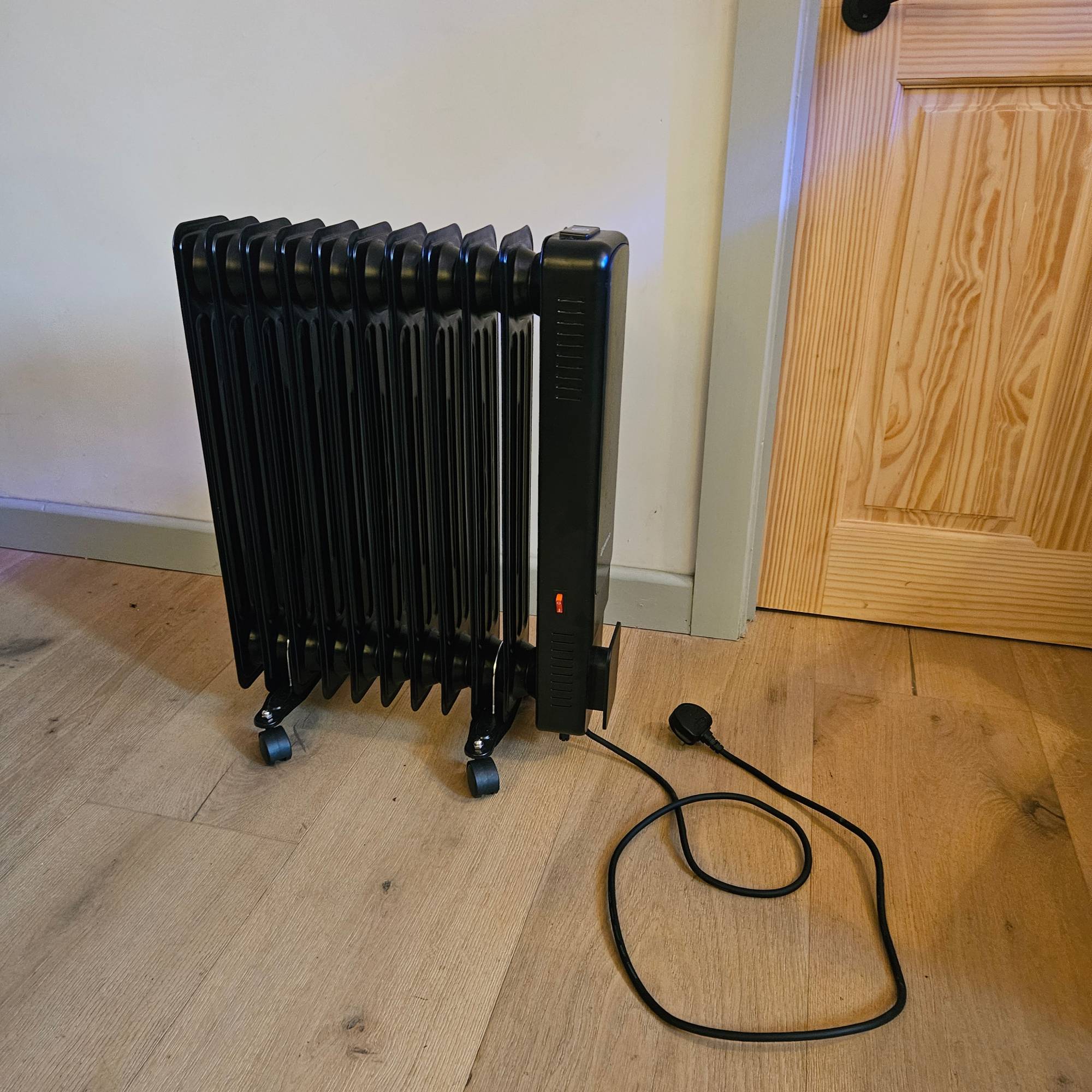 black unplugged oil filled radiator in white room with wooden floor