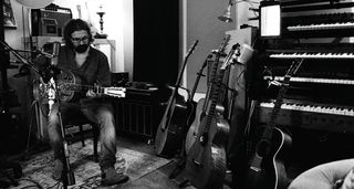 A black-and-white image of Jamie Dickson playing a resonator in the studio