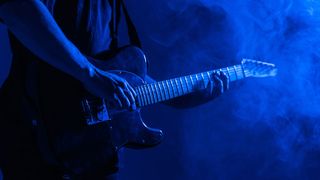 Male guitarist plays music in neon light with smoke.