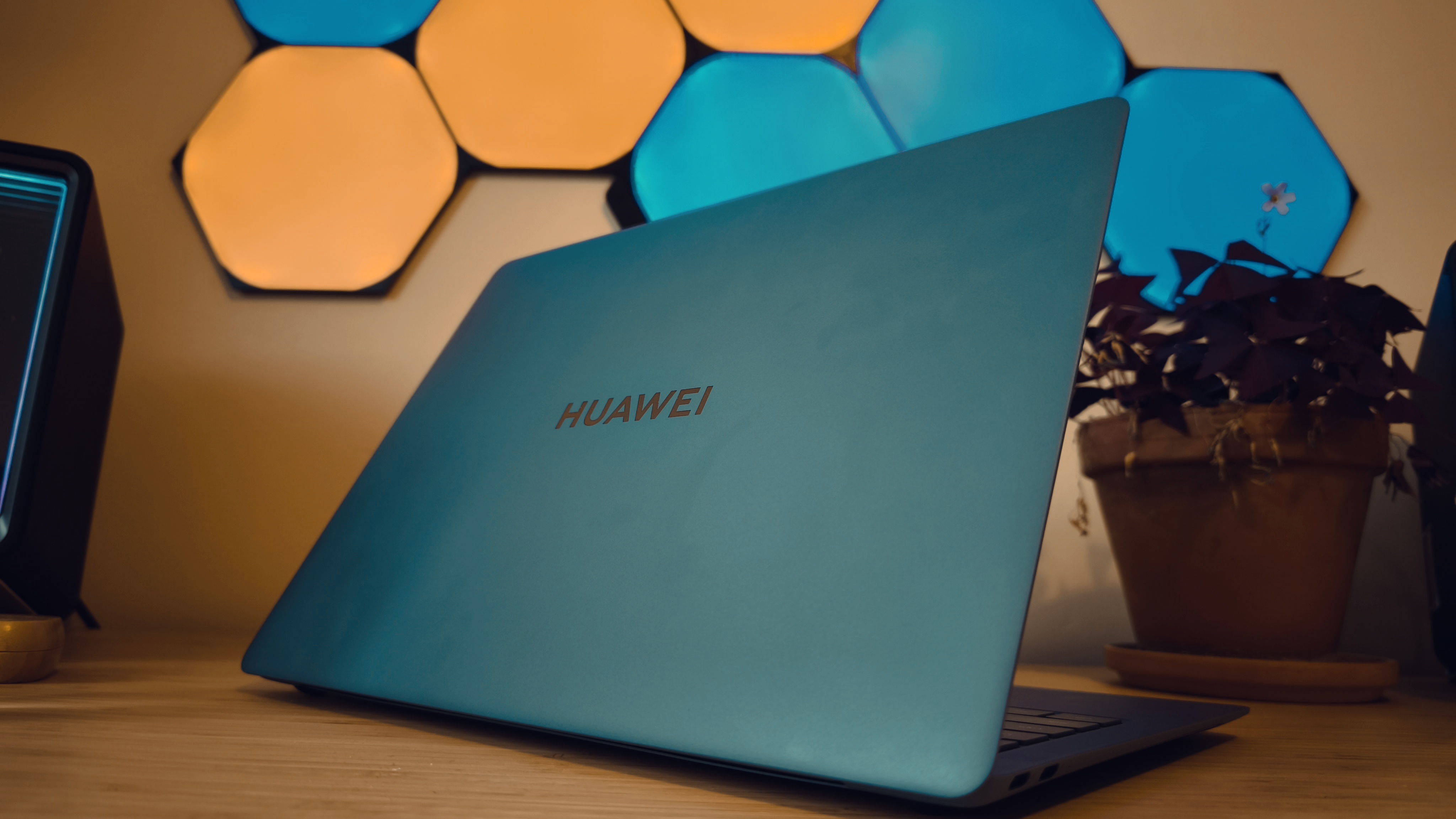 A blue Huawei Matebook X Pro laptop on a wooden desk, in front of blue and orange LED lights.