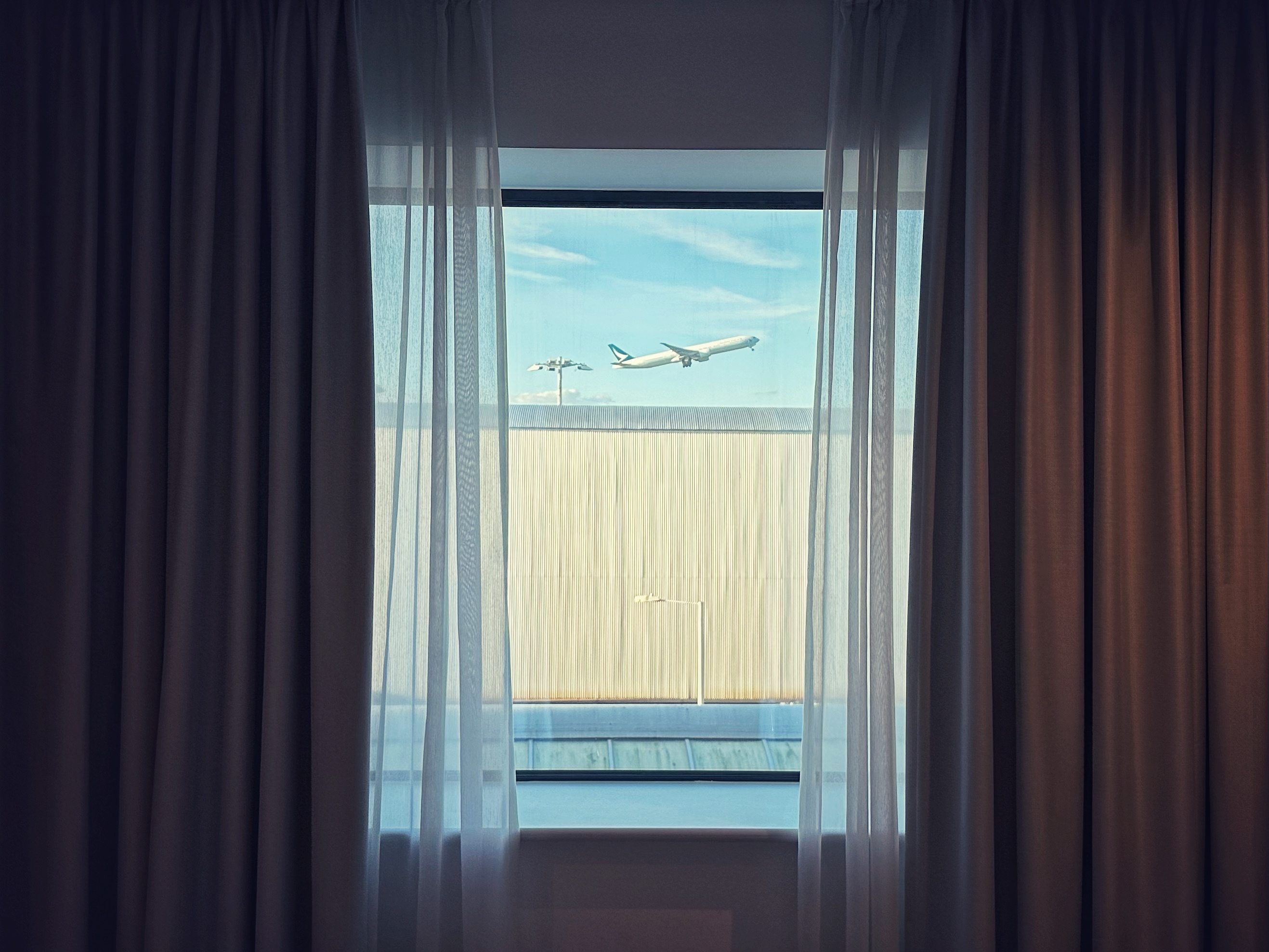 A window framed by curtains with a view of a plane taking off