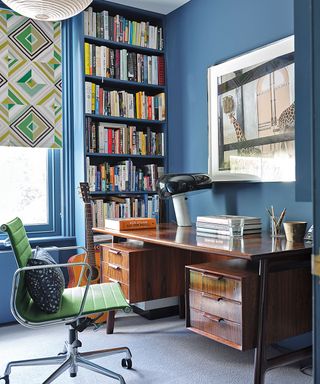 blue home office with large artwork, old wooden desk and green chair